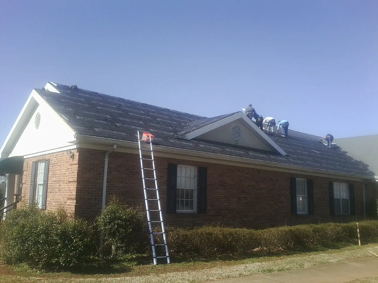 Crew tearing shingles off a brick ranch roof with a ladder set — Metal Roof Repair work by our crew in Grissom Arb
