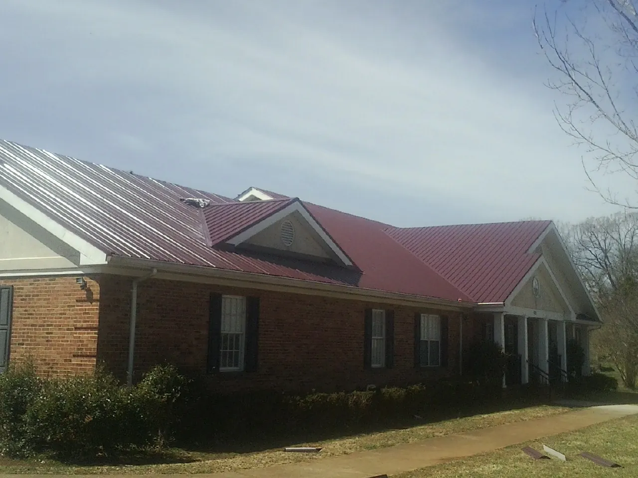 Red metal roof with gabled entries on a long brick building, from a Hail Damage Roof Repair job in Grissom Arb