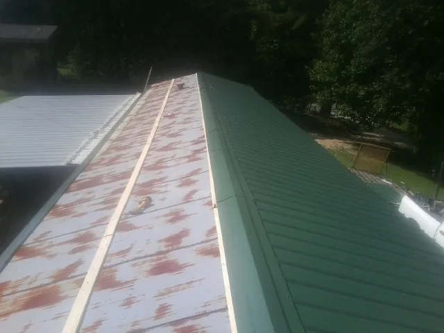 Old rusted panels beside newly installed green metal roofing — Wind Damage Roof Repair by Roofing Brothers in Grissom Arb