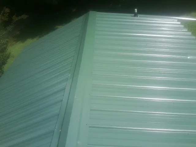 New green metal panels meeting at the ridge of a roof — Flat Roof Repair work by our crew in Grissom Arb