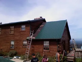 Green metal roof going on a two story log home with ladders set in Grissom Arb