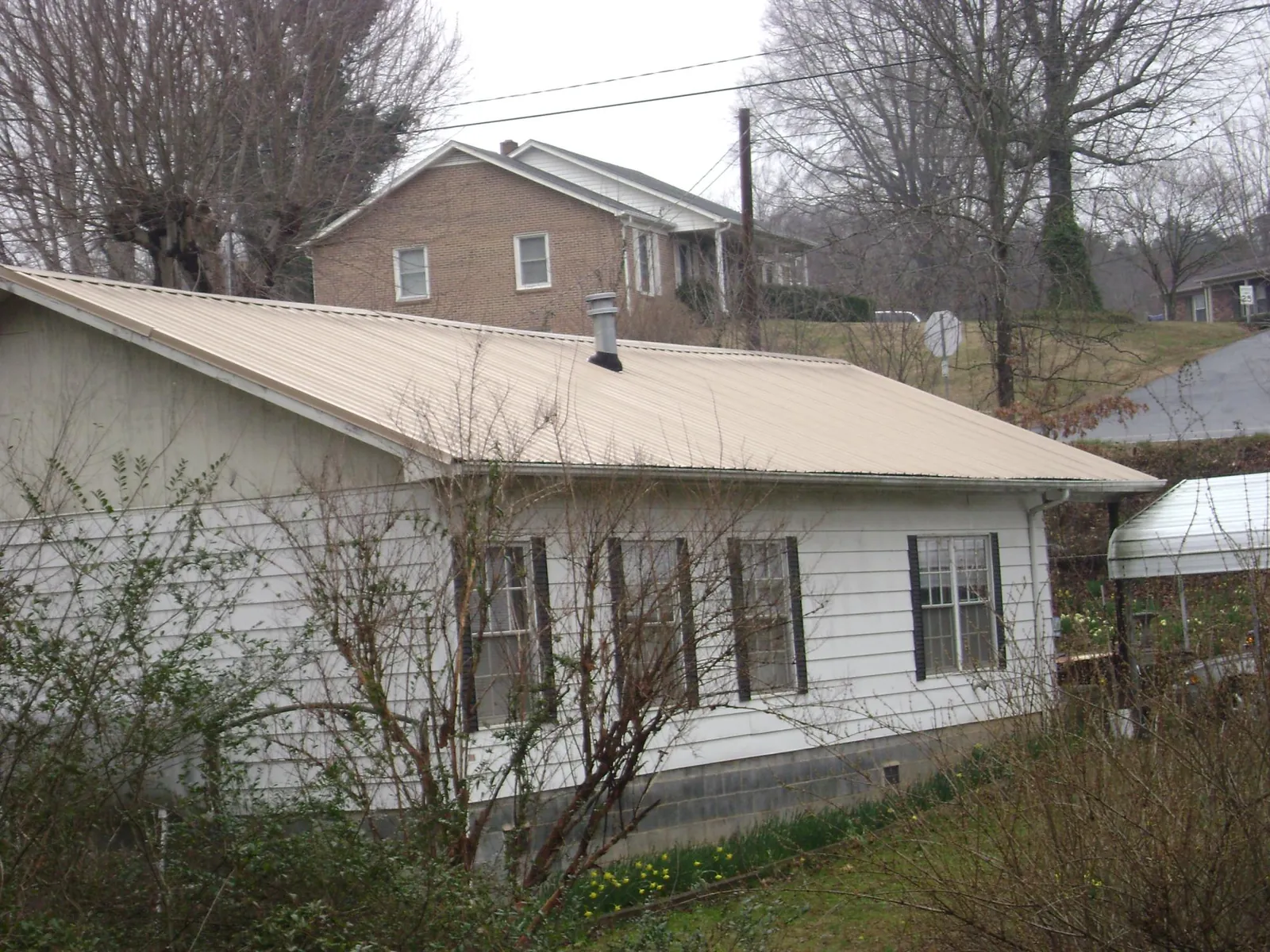 Tan metal roof on a white sided house set into a hillside — Commercial Roofing by Roofing Brothers in Grissom Arb